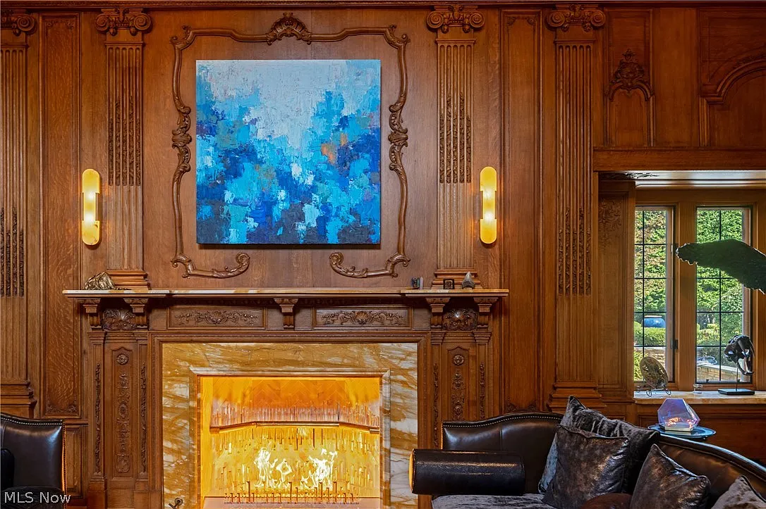 A fireside sitting area is arranged along one side, where a carved mantel frames the fireplace and leather seating creates a more intimate gathering point within the room. 