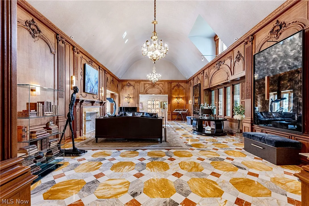 Overhead crystal chandeliers hang from a curved ceiling softening the hand-carved wood paneling along the walls and a patterned marble floor.