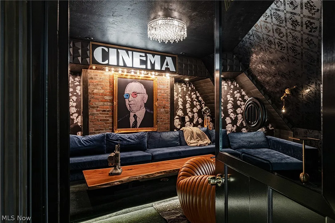 The private cinema features deep blue sectional seating that wraps around a long wood coffee table, while a black ceiling, glittering chandelier, and a black-and-white wallpaper of people watching a movie complete the design.