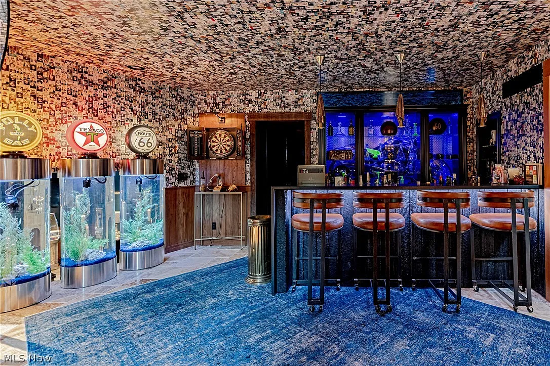 A full bar stretches across one side with leather stools pulled up to the counter, while three circular fish tanks sit off to the left.