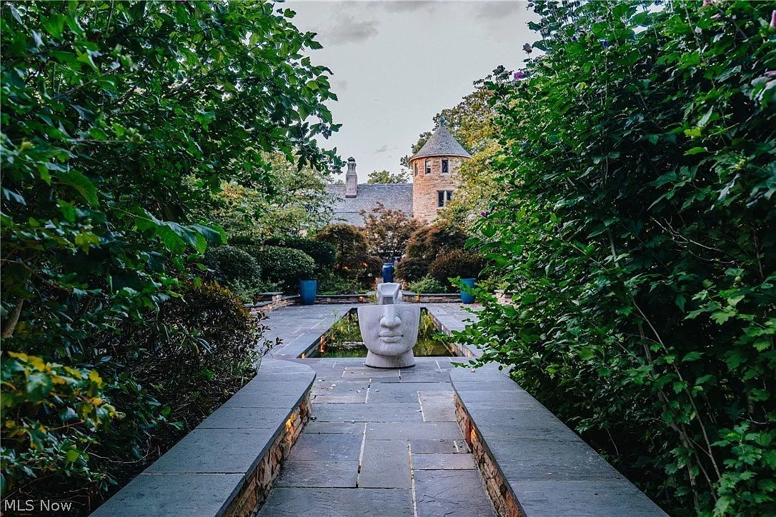 Stone paths lead deeper into the landscaping, narrowing between tall bushes before opening onto a garden courtyard. 
