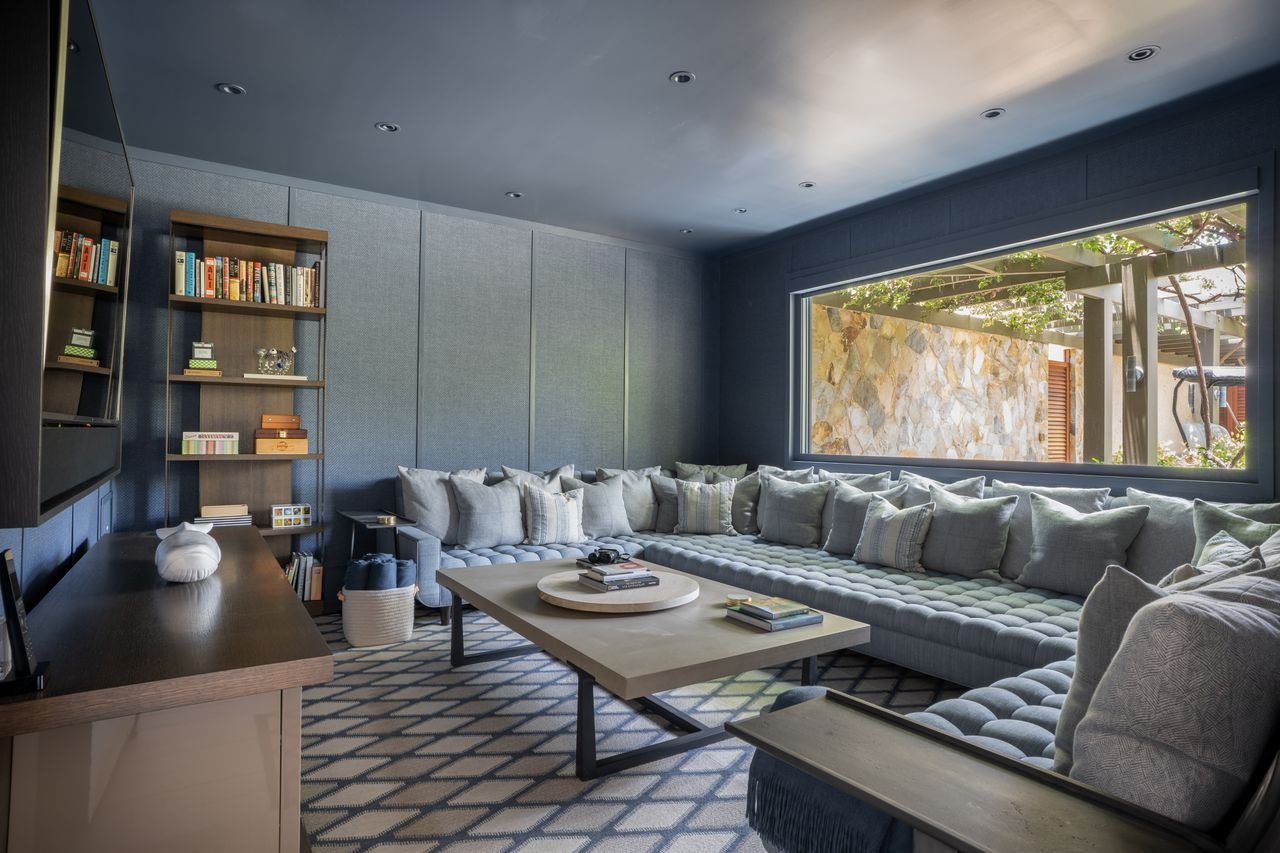 A deep wraparound sectional lines the perimeter to face a mounted TV all surrounded by dark wall panels.