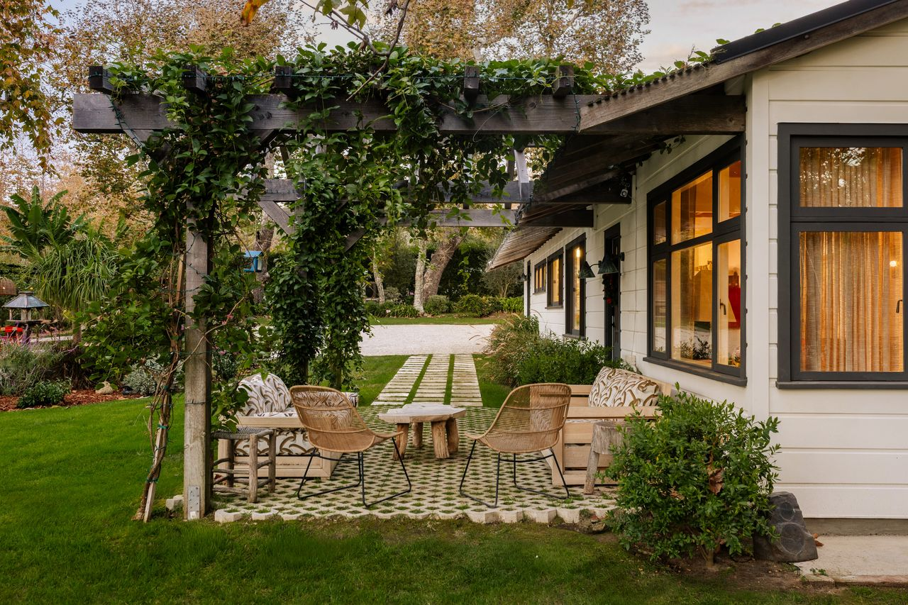 A path leads toward the front entrance, where a vine-covered pergola extends from the house over a small patio