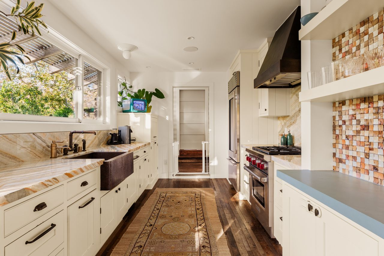 White cabinetry keeps the palette light, while the stone’s layered veining adds warmth around the dark brown farmhouse sink and high-end appliances. 