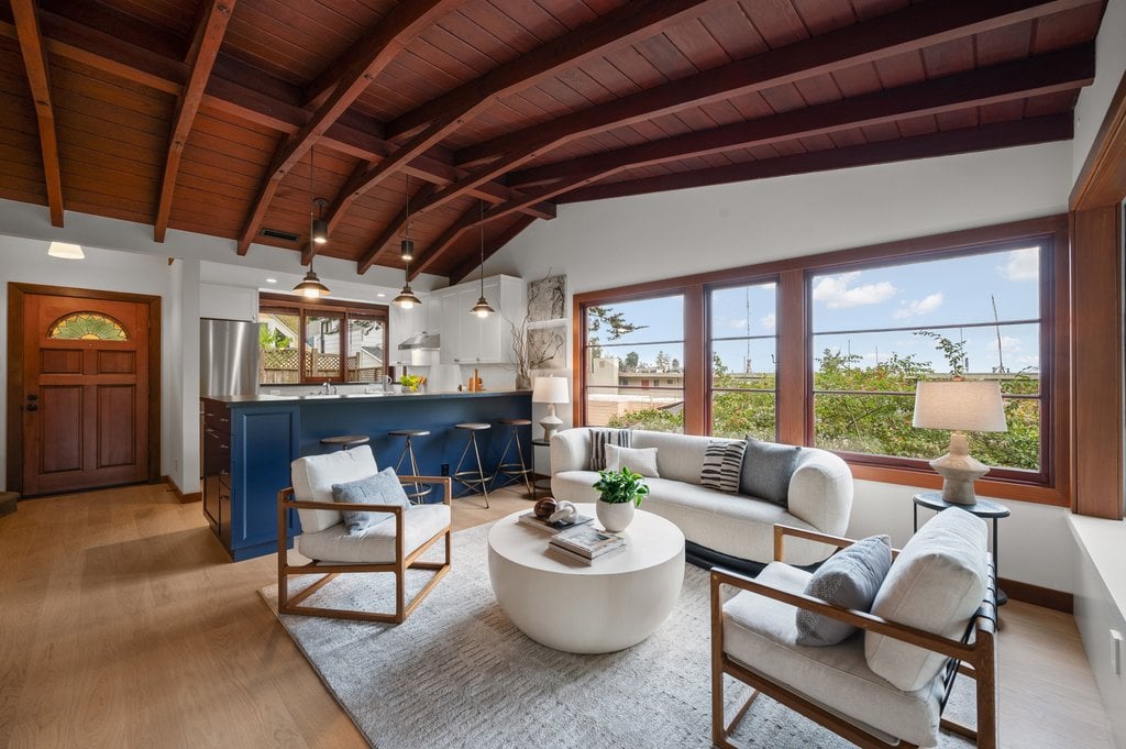 The living area sits against a wall of large windows with natural wood trim that look out to the surrounding greenery.