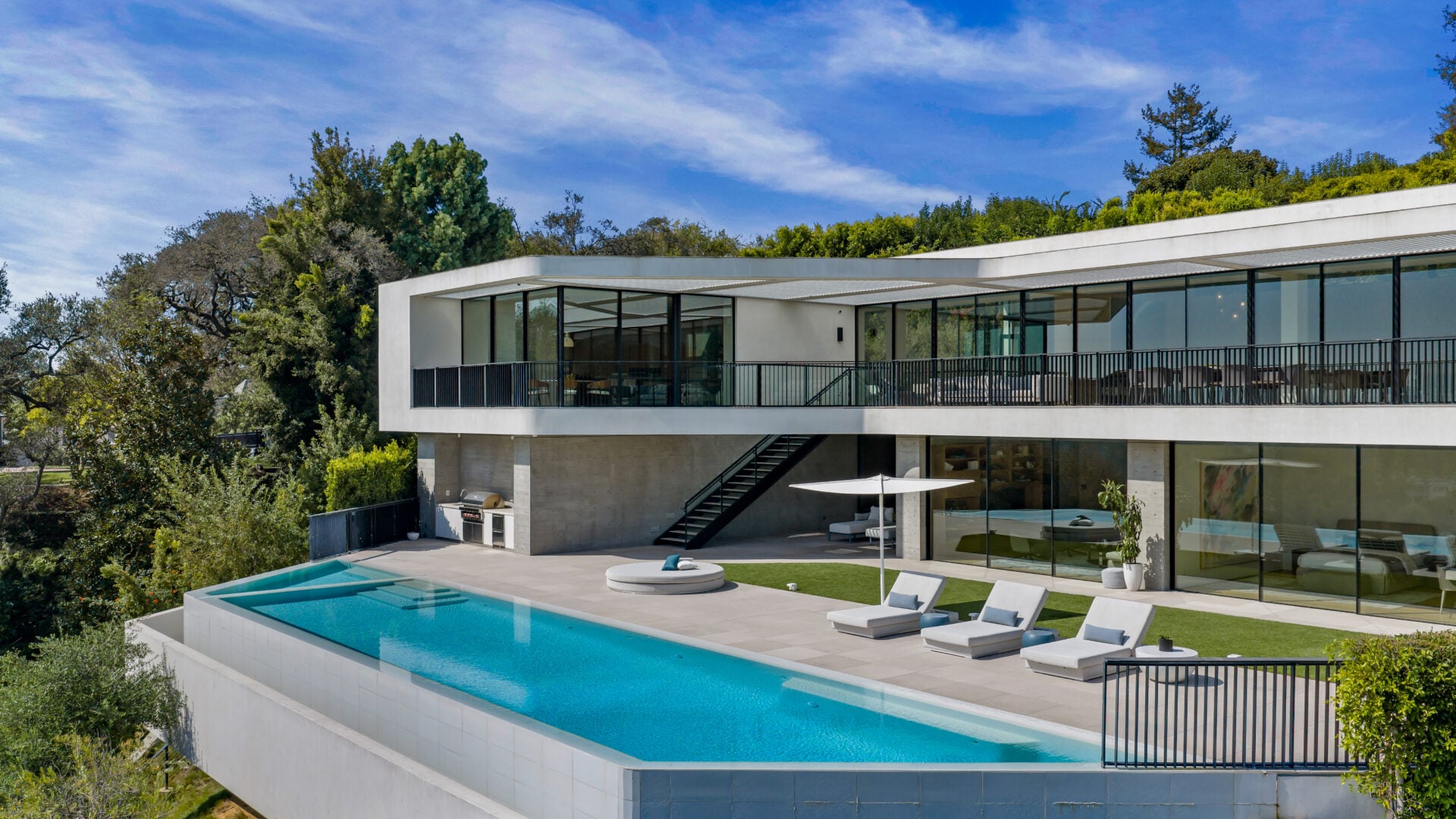 The infinity-edge swimming pool stretches along the outer edge of the property with an integrated spa positioned at one end. 