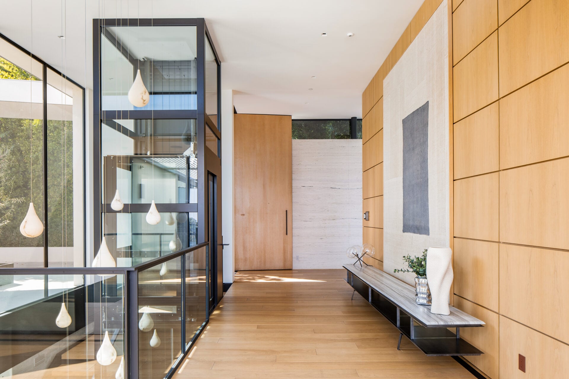 The private entrance opens to a central hallway where a glass-and-steel staircase rises through all three levels of the home. 