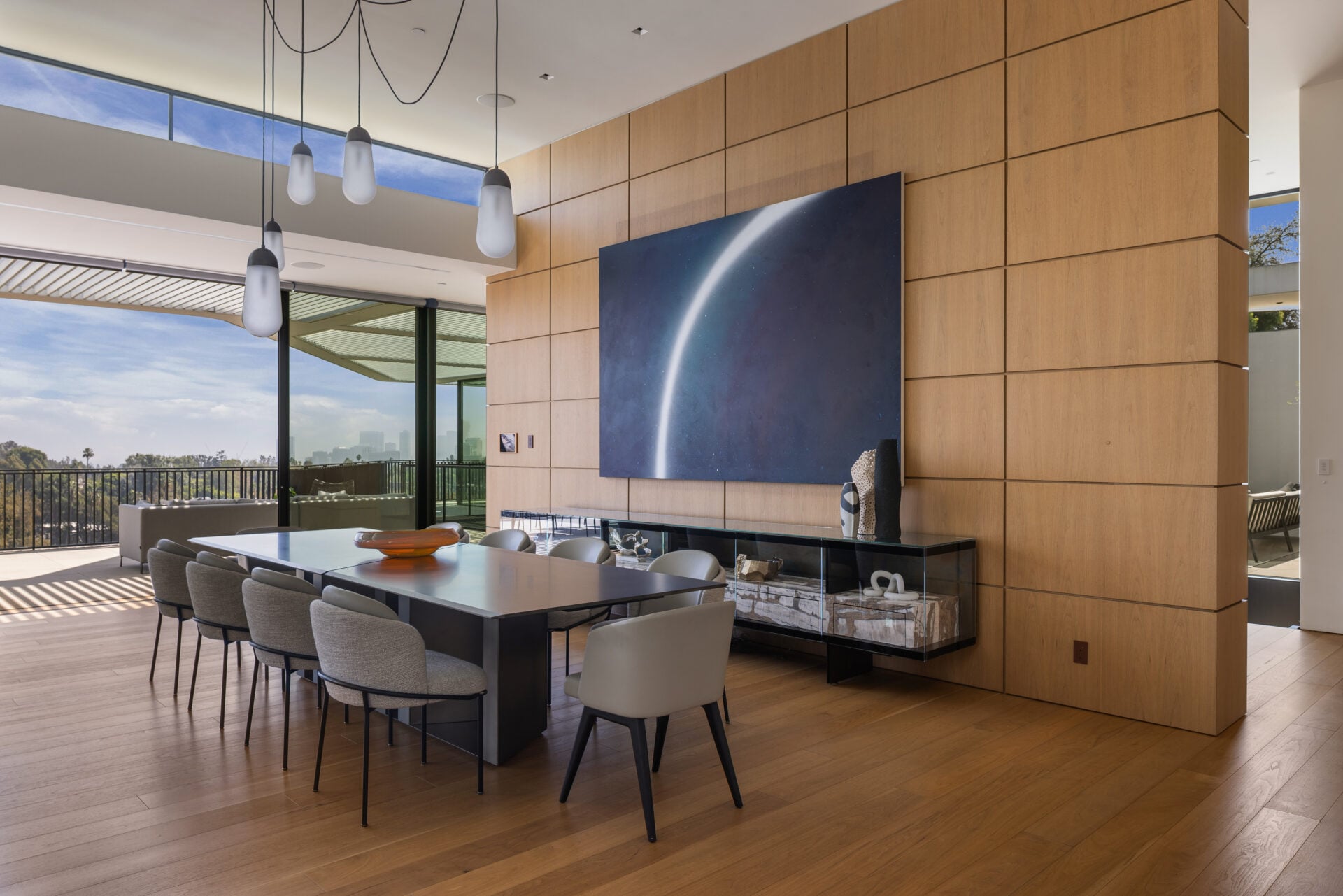 The dining room is set against a floor-to-ceiling wood-paneled wall, with a long table positioned beneath a cluster of suspended pendant lights.