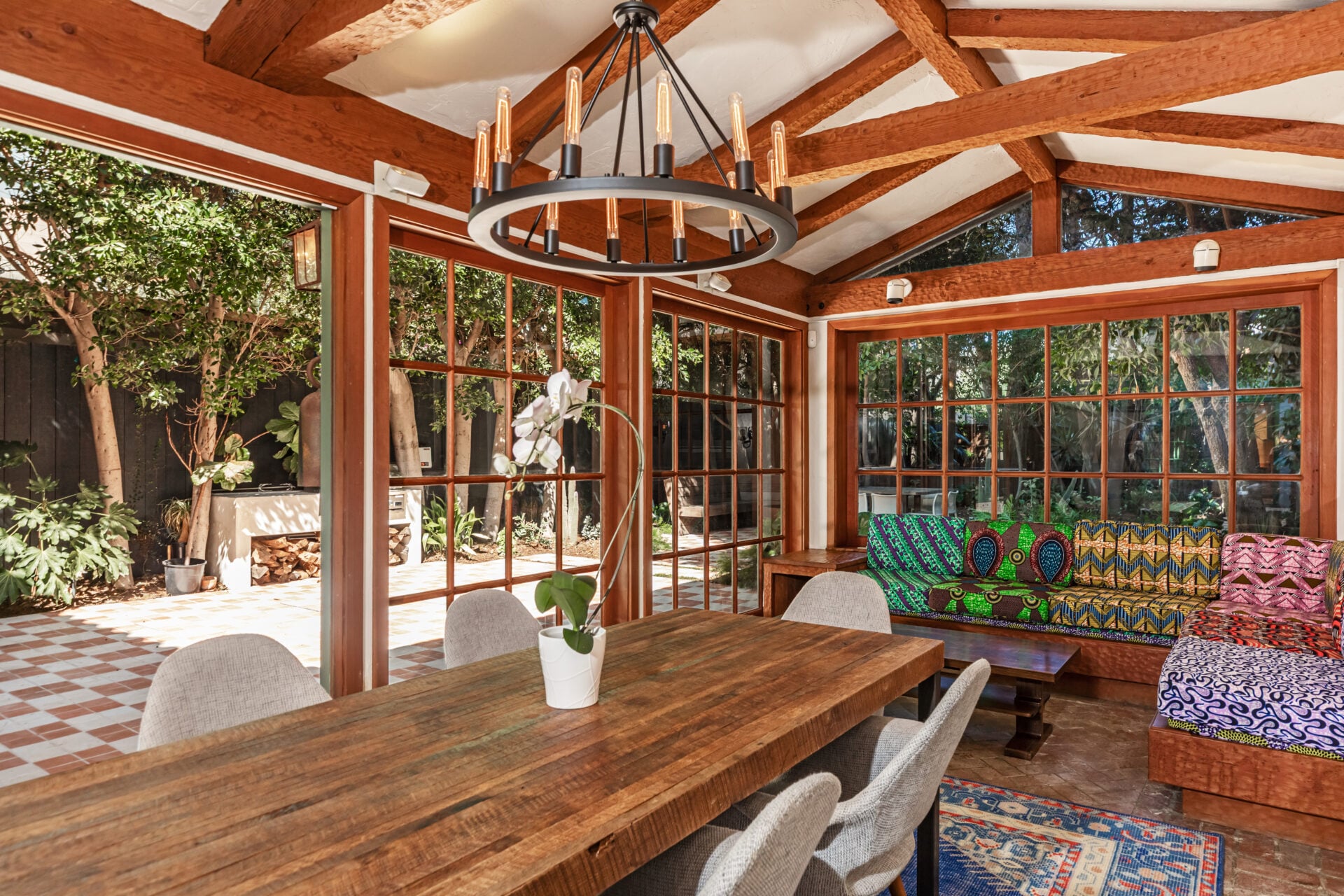 A long table sits beneath exposed trusses and a circular chandelier, while built-in bench seating fills the far corner.
