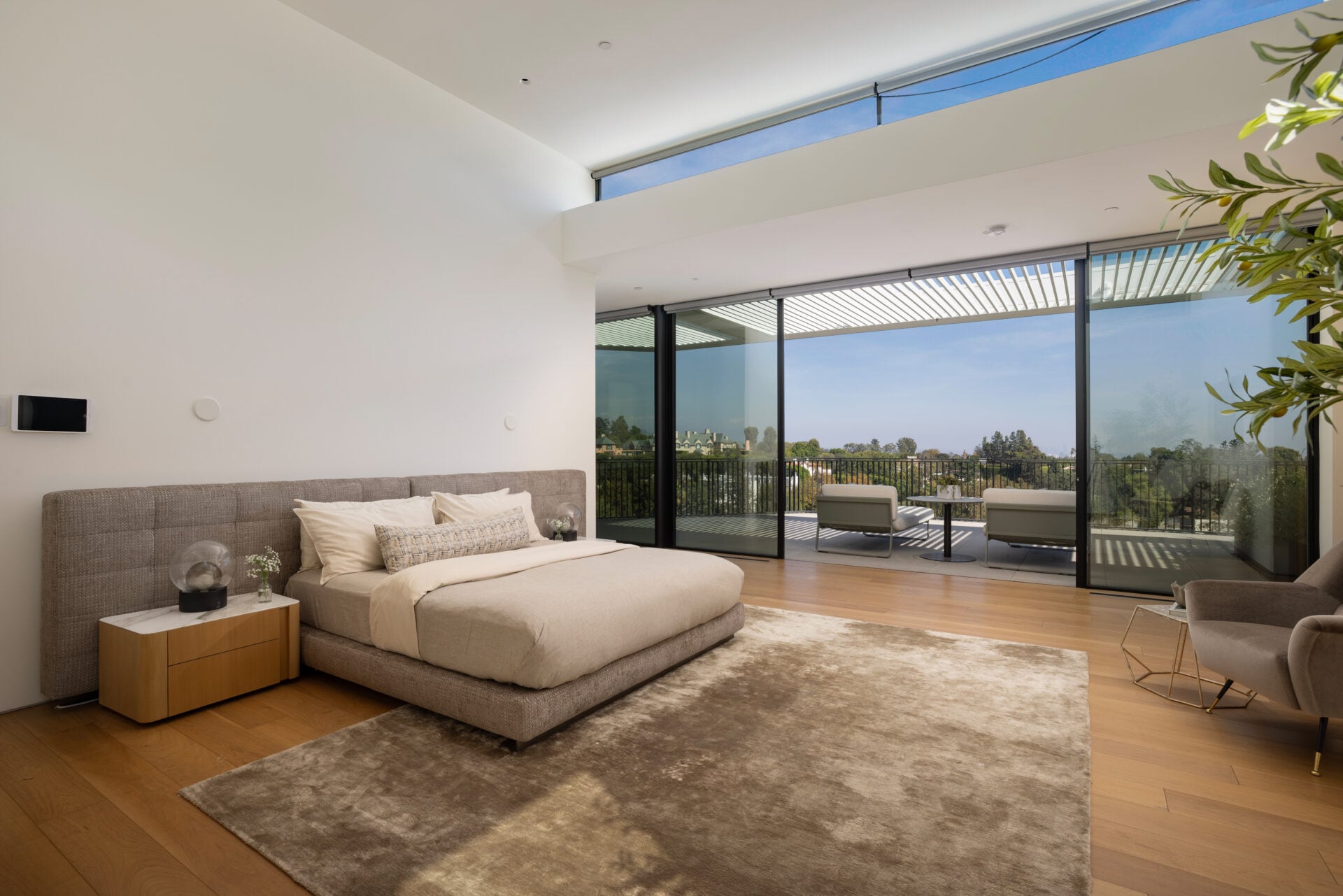 The main-level suite opens beneath a high ceiling, with sliding doors extending the bedroom onto a private terrace. 