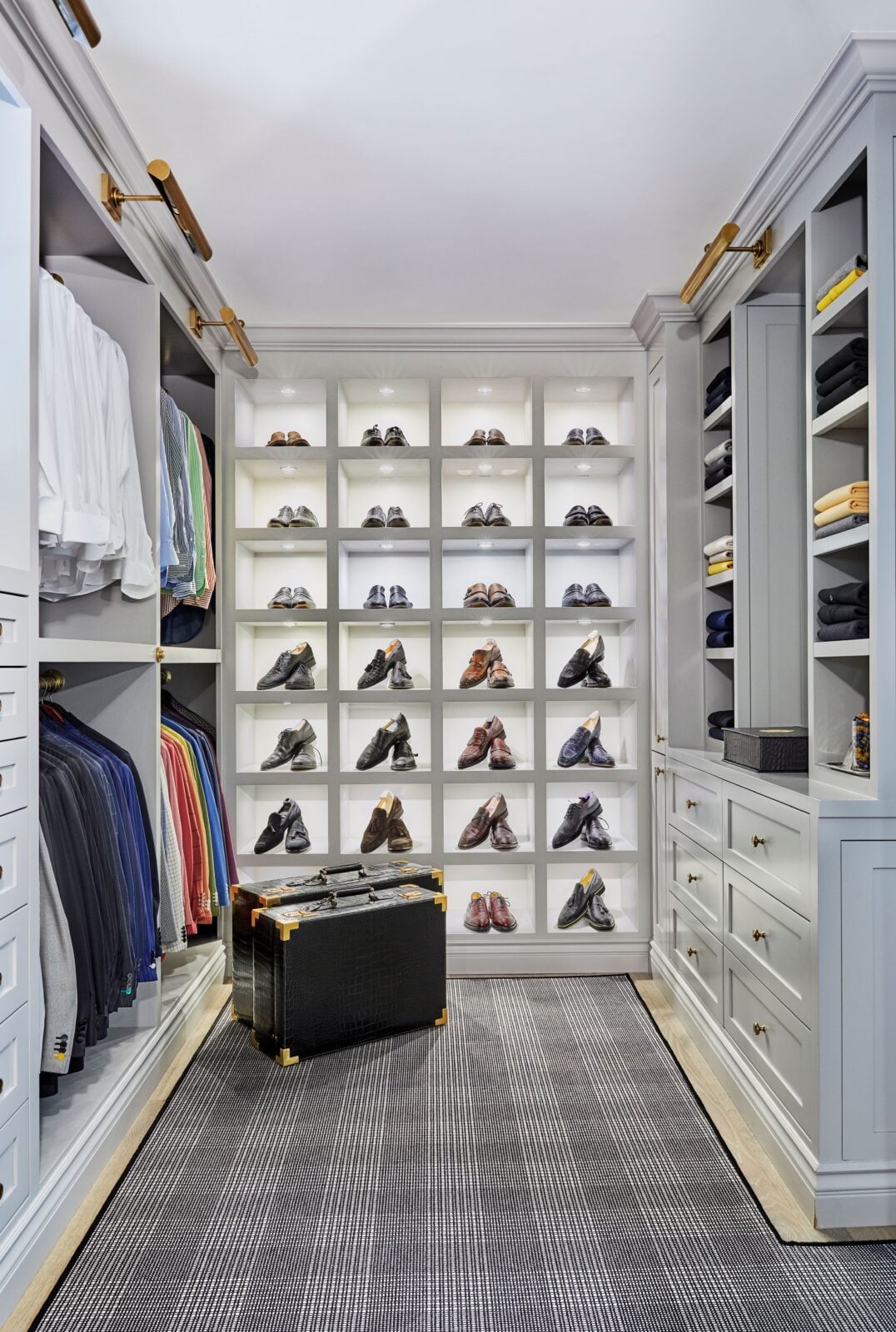 The closet is built with custom cabinetry on all sides, with dedicated hanging storage, drawers, shelving, and a full wall of individually lit shoe cubbies at the far end.