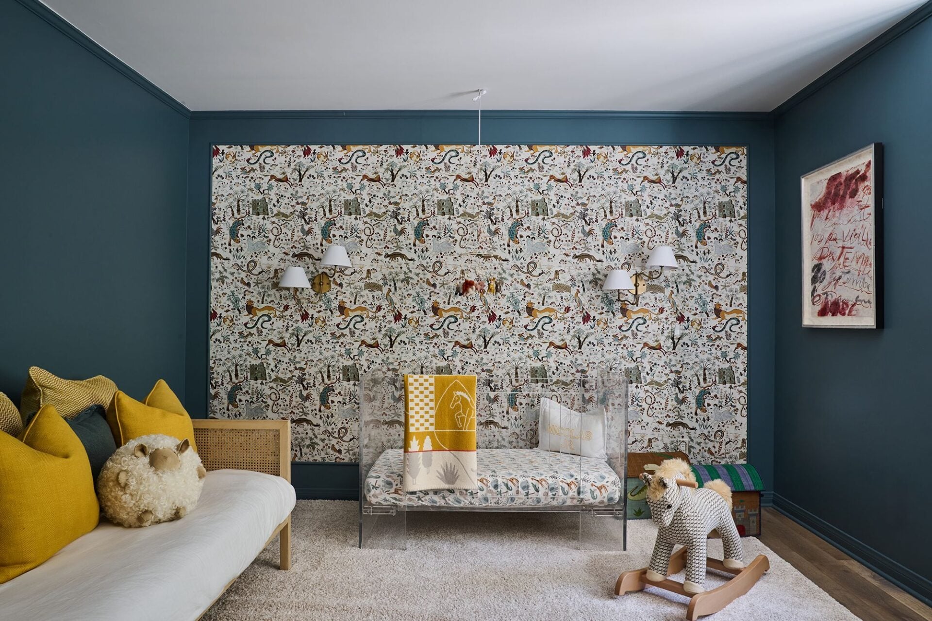 The room is furnished with mustard-colored pillows, a cane-framed daybed, and an acrylic crib.