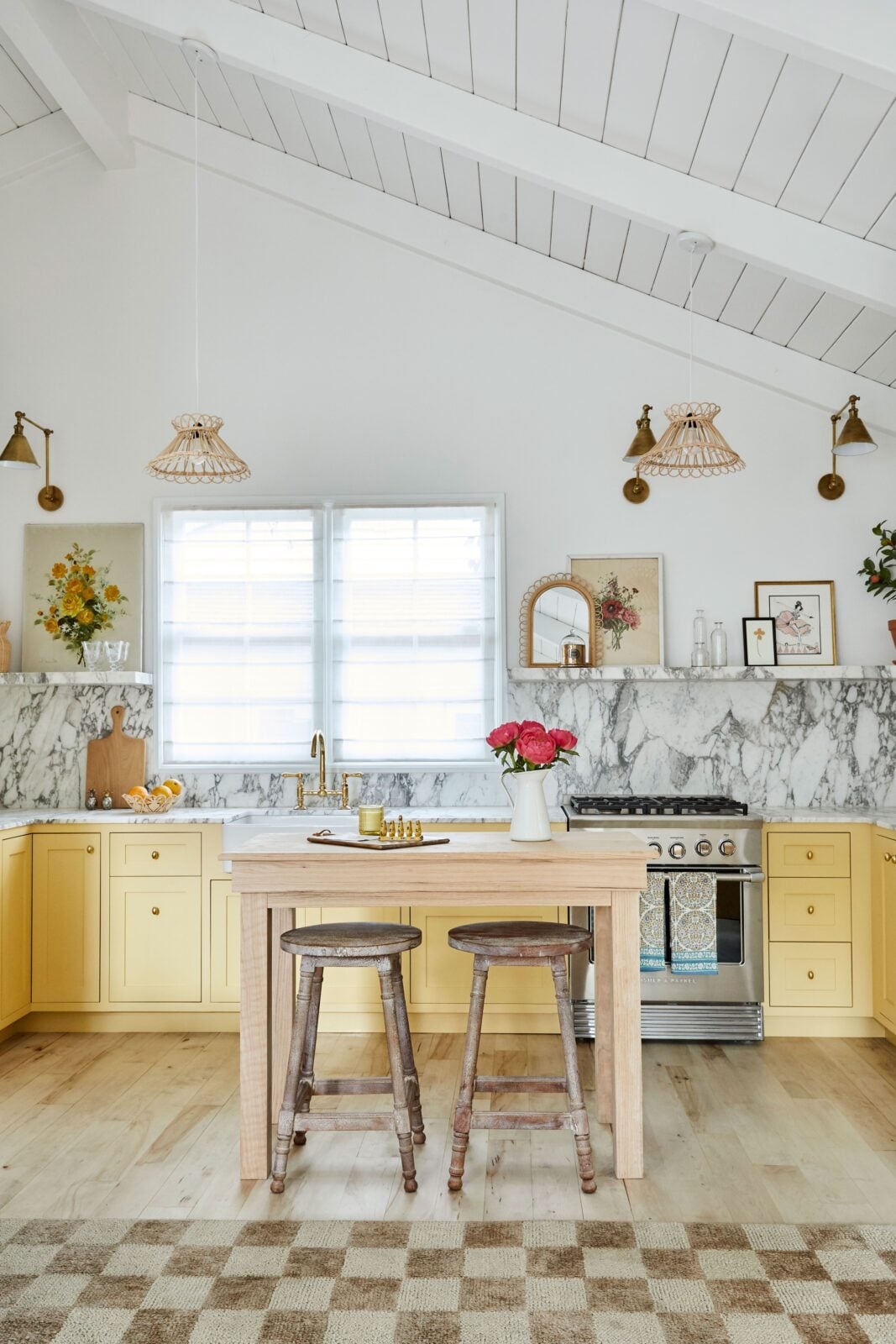 The kitchen has pale yellow cabinetry, marble counters and backsplash, and a small center island for casual dining.