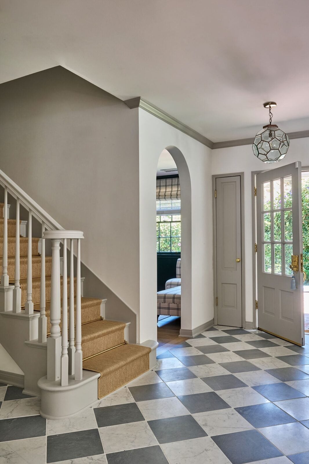 The front door opens across a checkerboard stone floor with the staircase rising along one side.