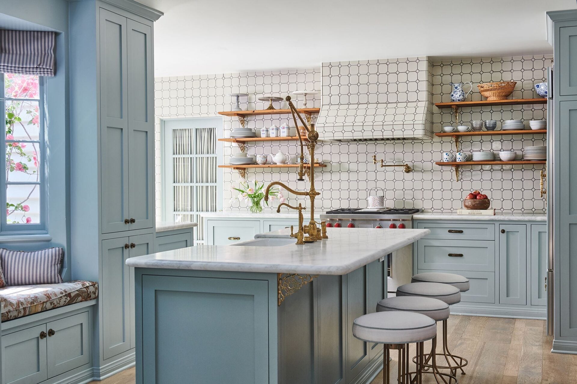 Pale blue cabinetry wraps the room, while open wood shelving and a geometric tile backsplash frame the stove.