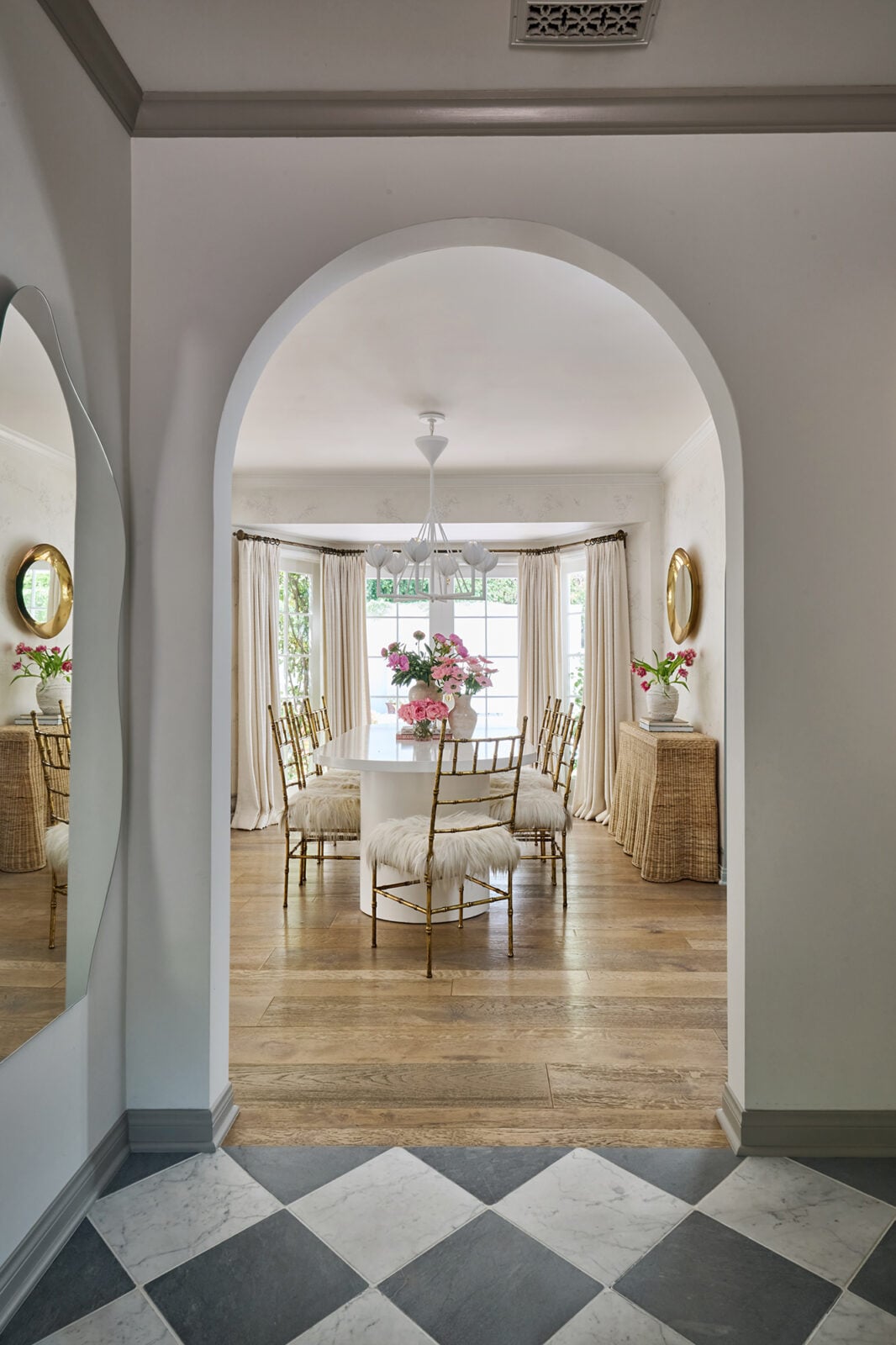 The formal dining room sits within another arched opening, with a long white table running through the center of the room in front of a bay of tall windows.