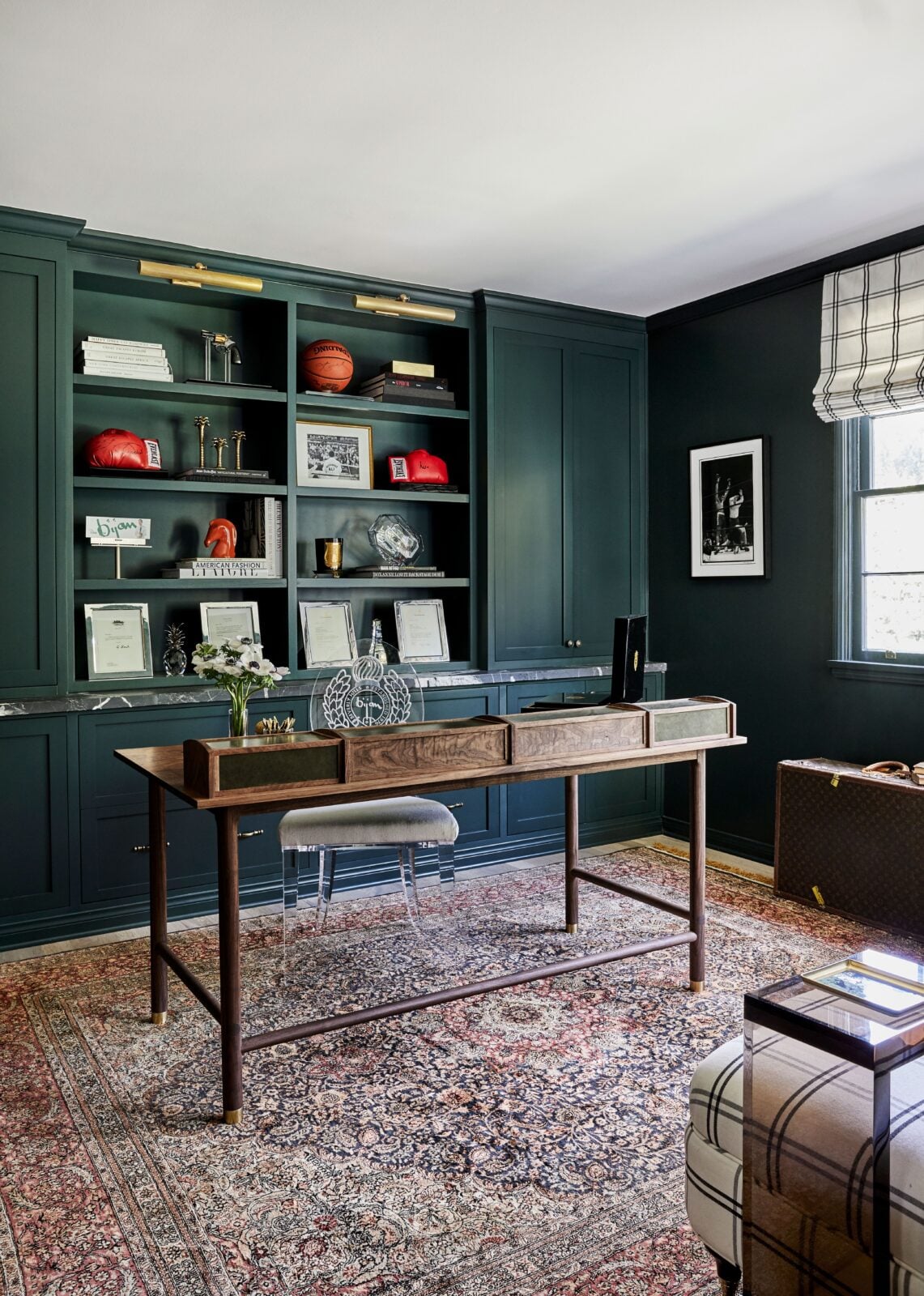 A garden-facing office is painted in a deep green with bookshelves built into the center of upper and lower cabinetry along the back wall.