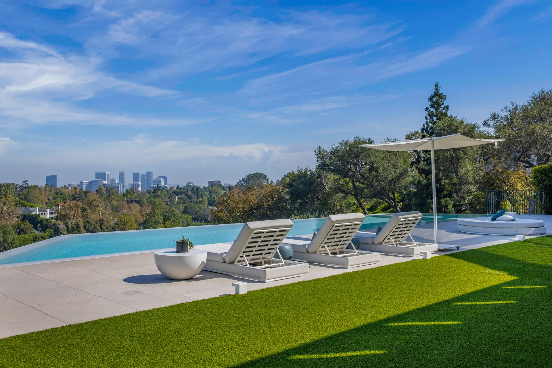 Lounge areas and strips of turf sit behind the water, while the disappearing edge opens to the surrounding treetops and distant skyline.