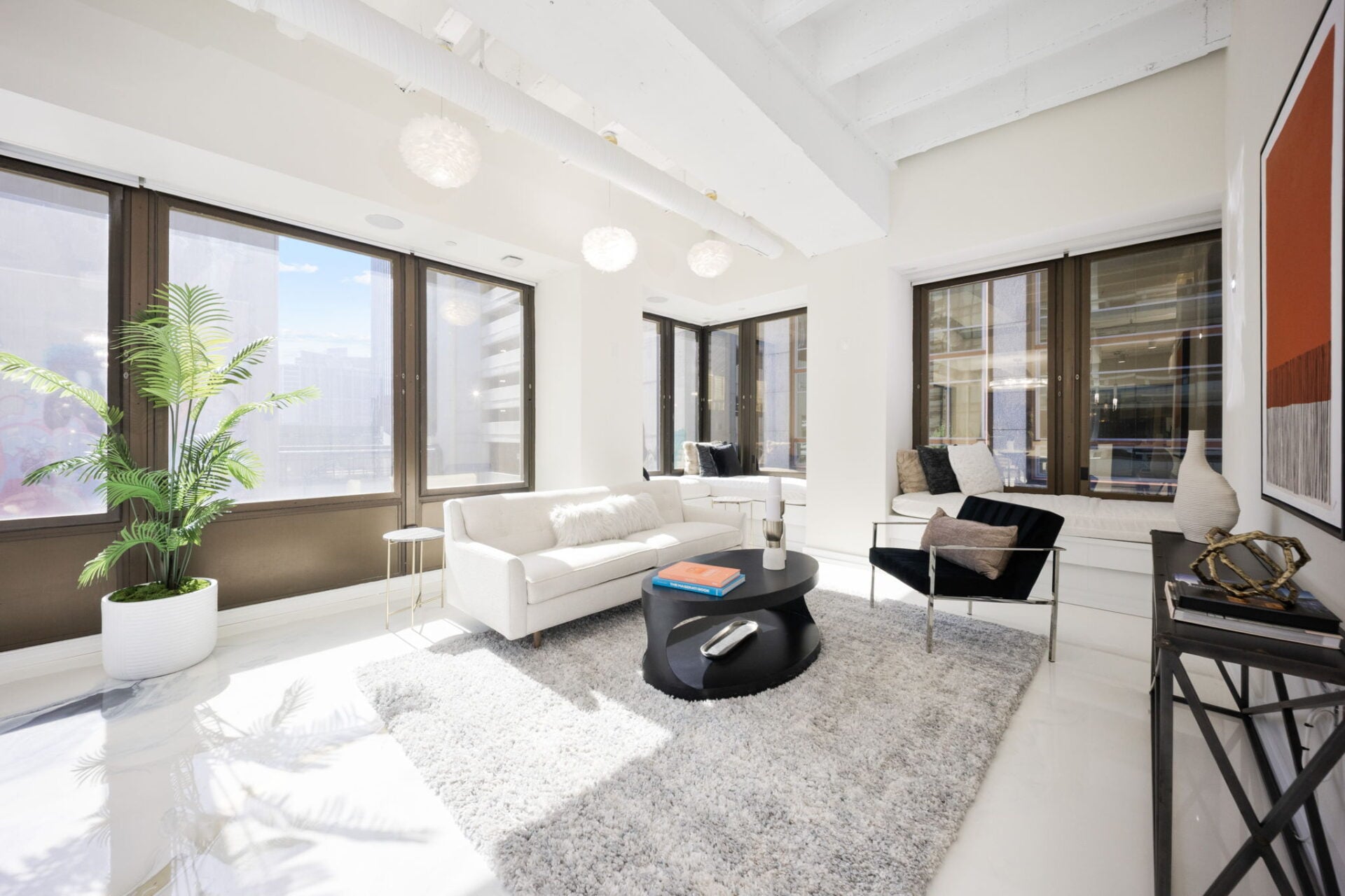 A white sofa faces a black lounge chair across a circular coffee table, while built-in window seats wrap the far wall.