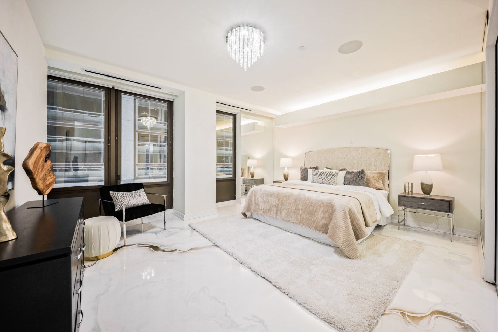 A spacious bedroom with the bed sitting across from a small sitting area beside the glass windows.