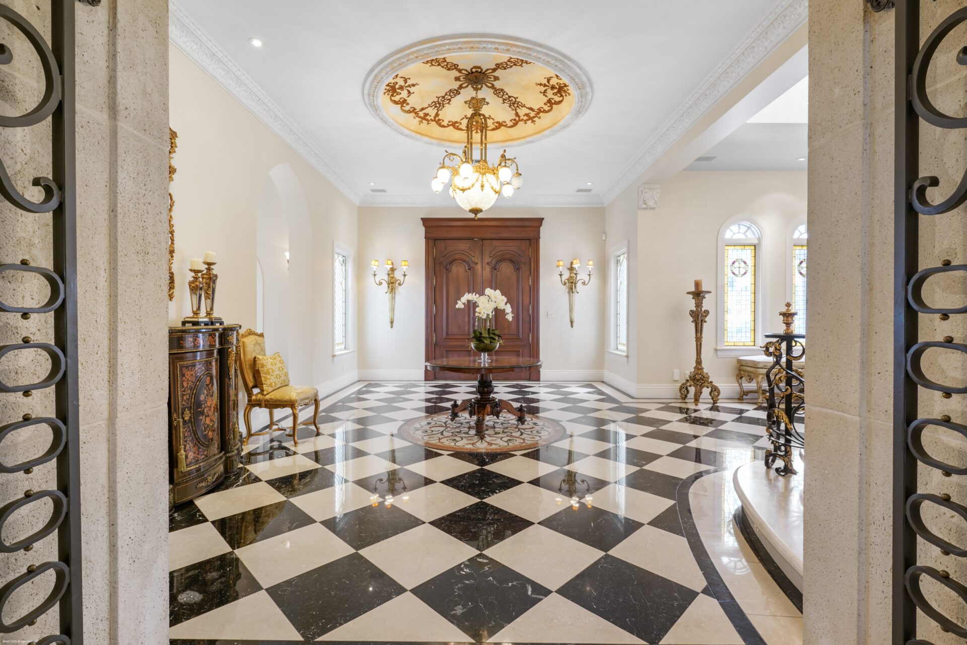 The foyer opens across glossy black-and-white checkered floors beneath a central chandelier.