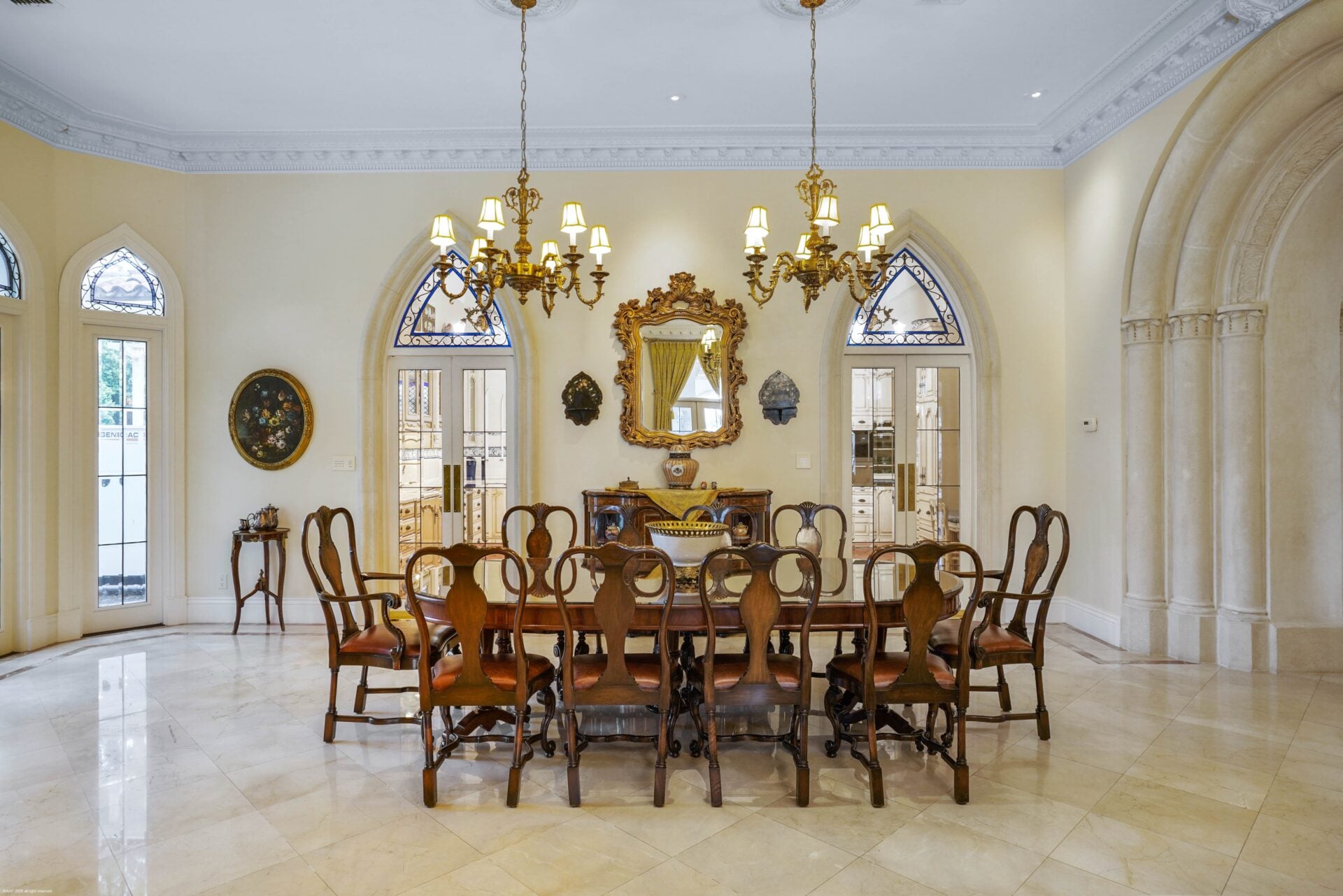 The formal dining room opens past a columned archway with pale stone flooring extending beneath a long wood table.
