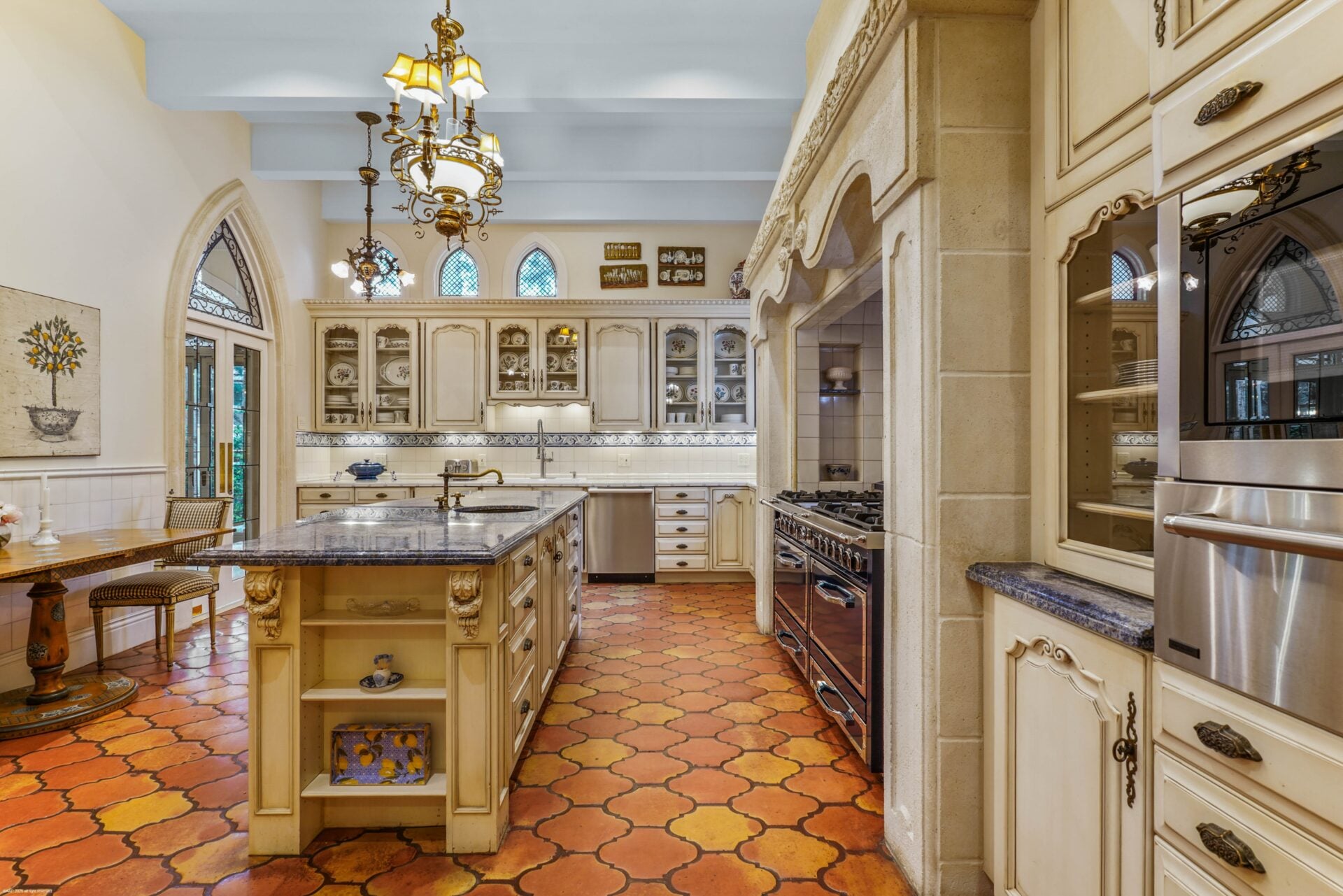 The kitchen's floors become a patterned terracotta running beneath cream-colored cabinetry and dark stone counters.
