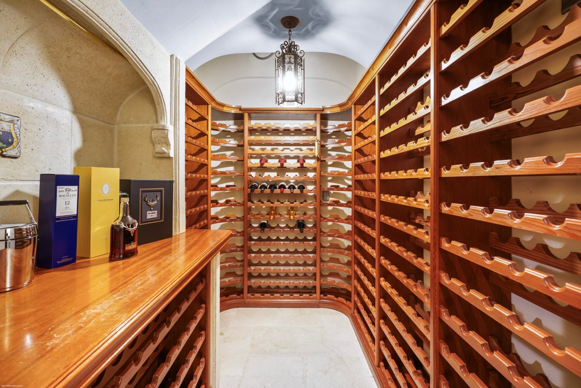 The wine cellar has custom wood racks lining nearly every inch of the wall, with a long counter on the left breaking up the rows.