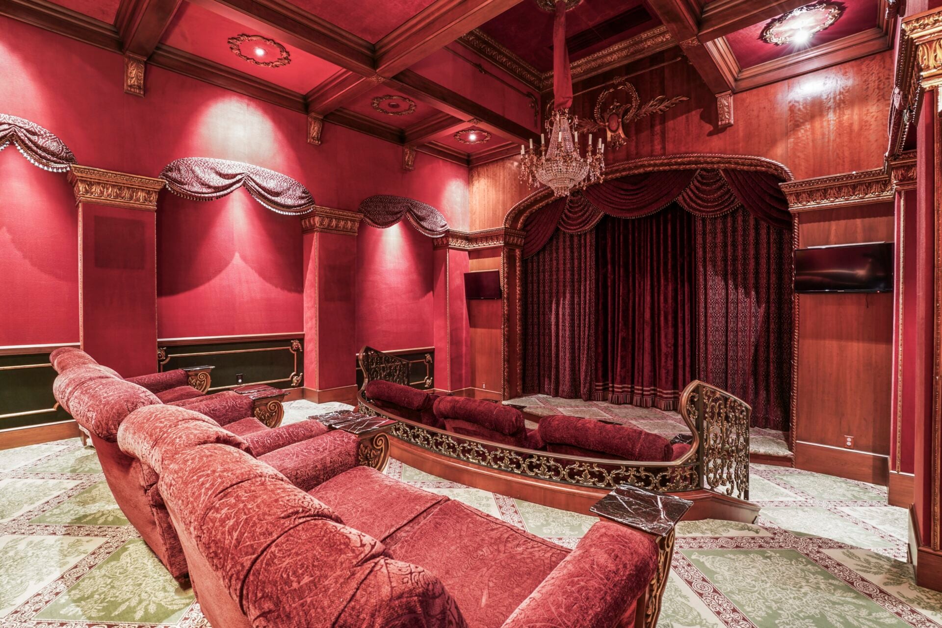 Home theater with deep red walls, matching curtains, and rows of red velvet theater seating facing a large screen at the front.
