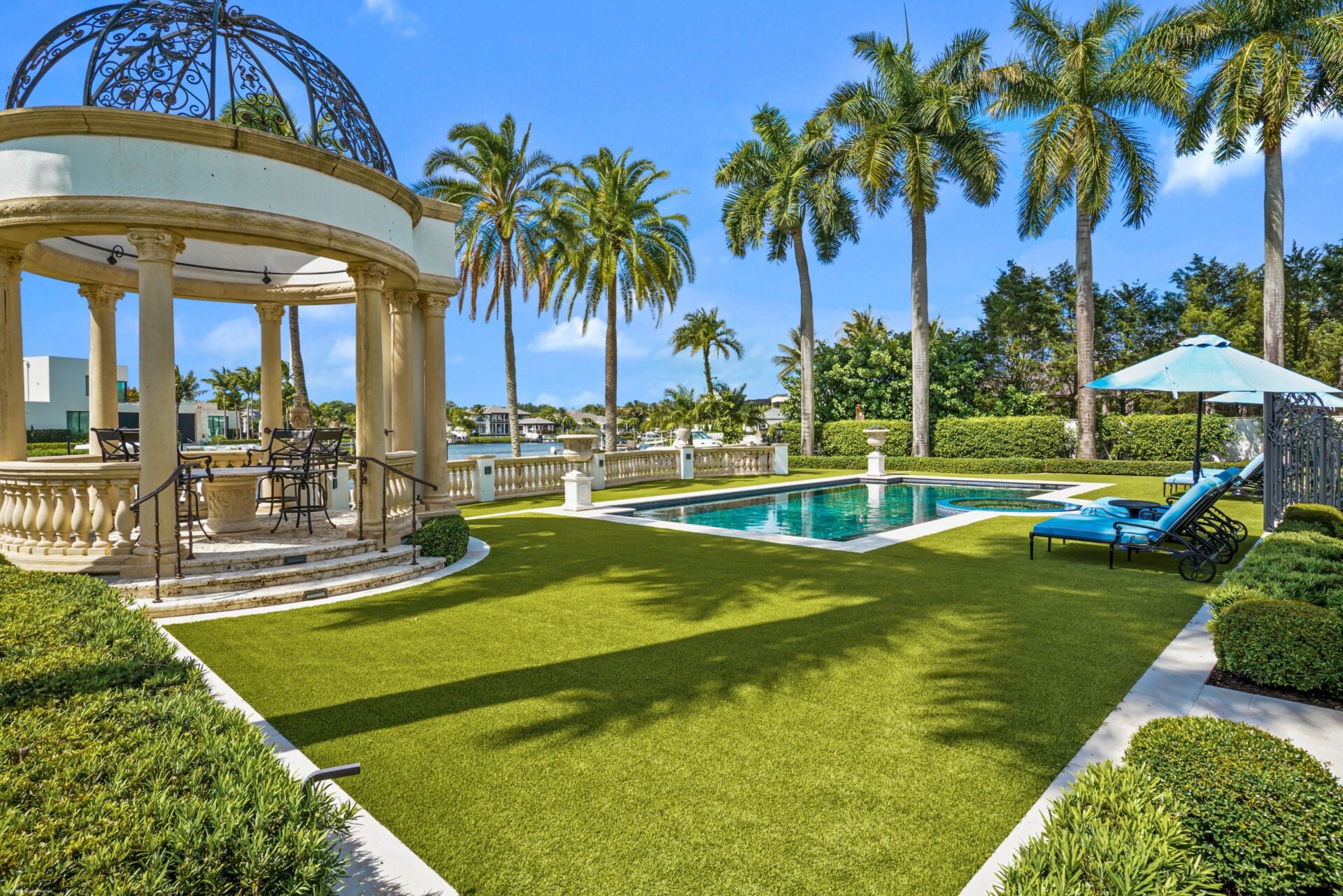 A separate dining gazebo stands off to one side, creating another gathering space beside the pool with the waterfront as the backdrop.