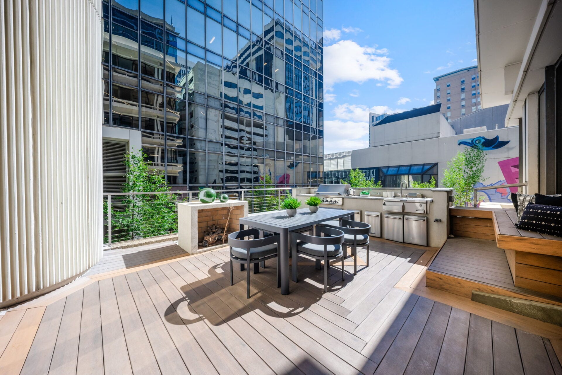 A dining table sits near the center, while built-in bench seating runs along the windows and a low outdoor fireplace is positioned along the metal railing.