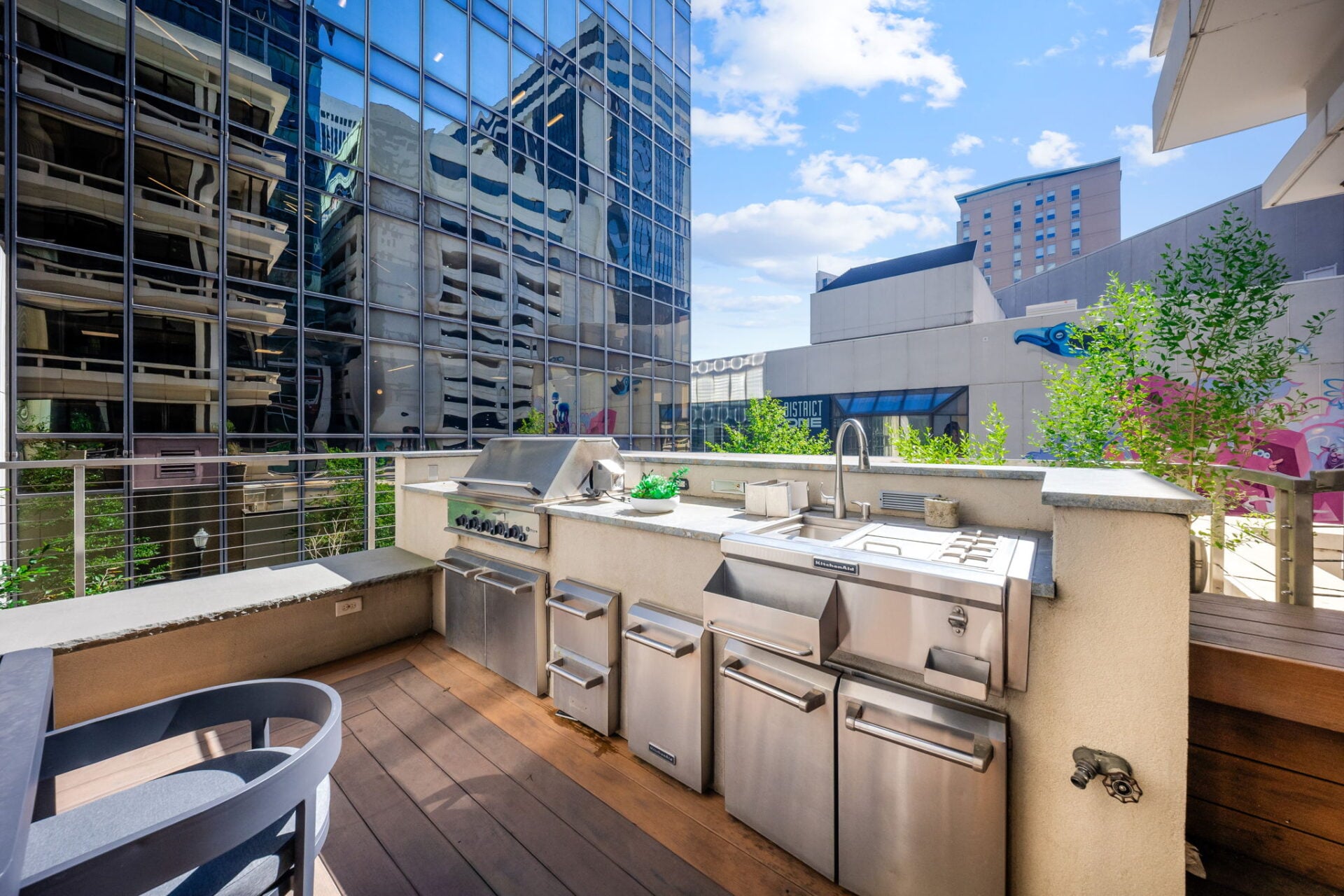 Along the back edge, a built-in outdoor kitchen features a large grill, sink, cooktop, and stainless-steel storage.