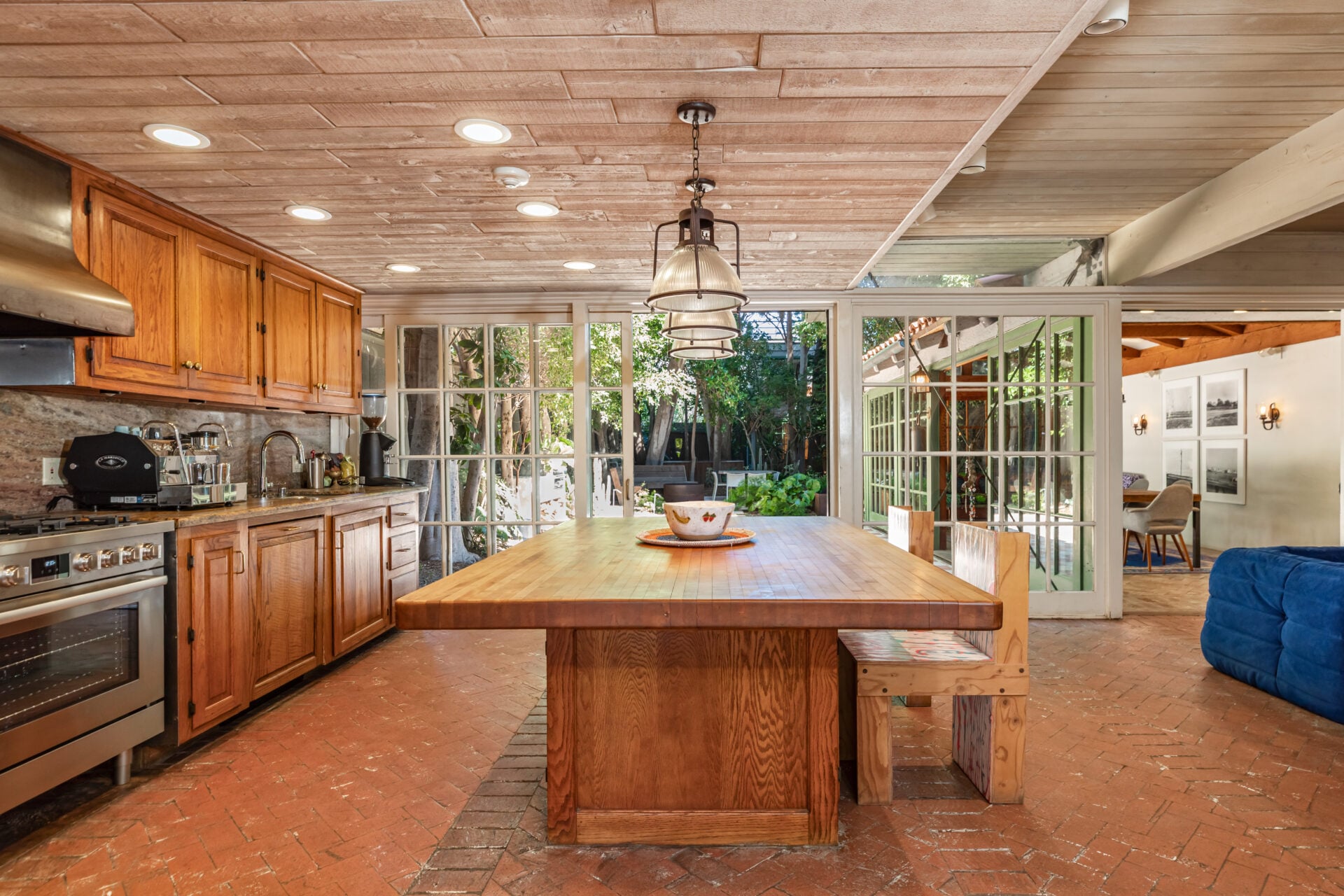Wood cabinetry lines one side of the room, while a large butcher-block island stretches through the center beneath a row of pendant lights. 
