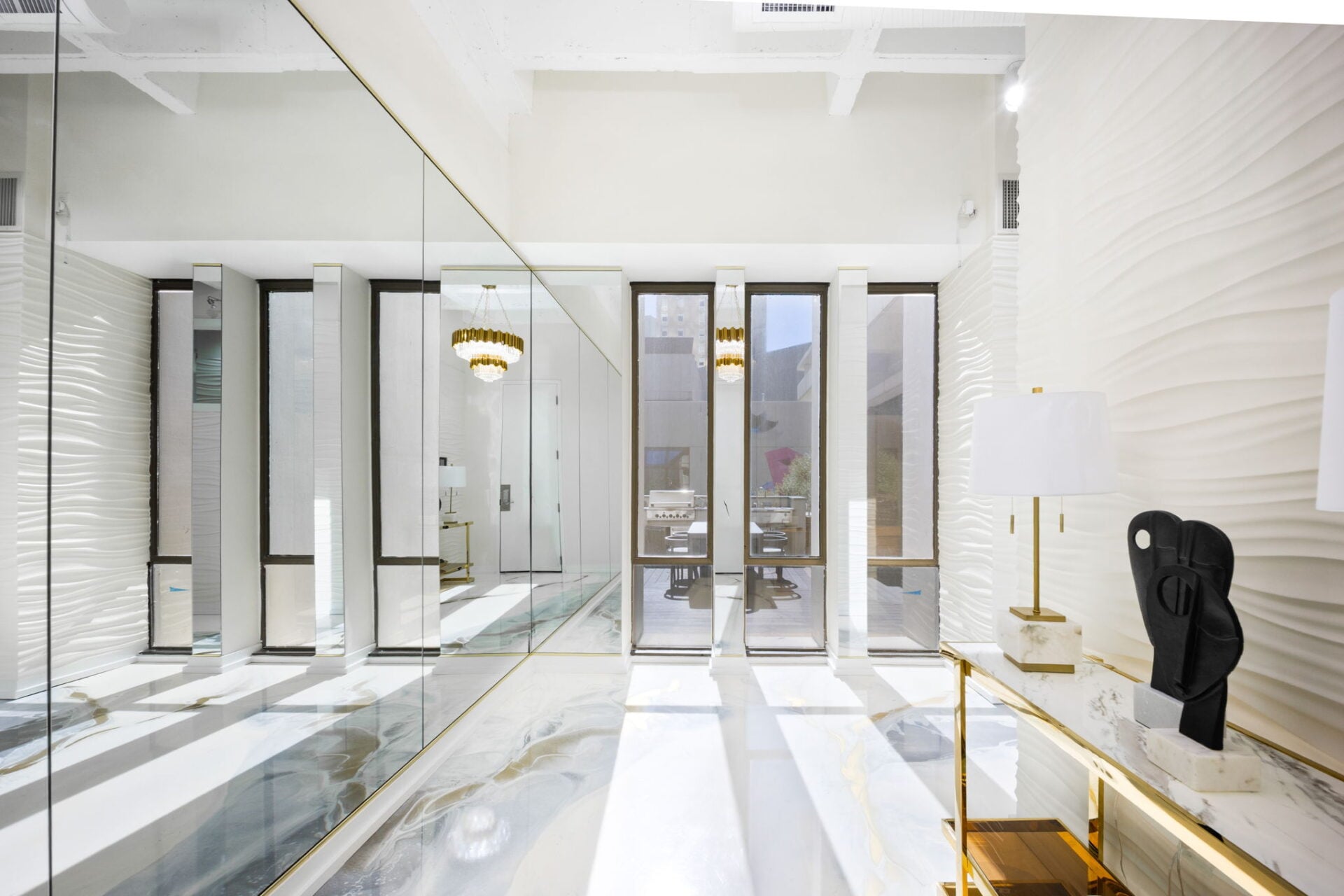 Polished marble flooring with gold and gray veining draws you through the long entry toward tall windows overlooking the terrace at the far end.