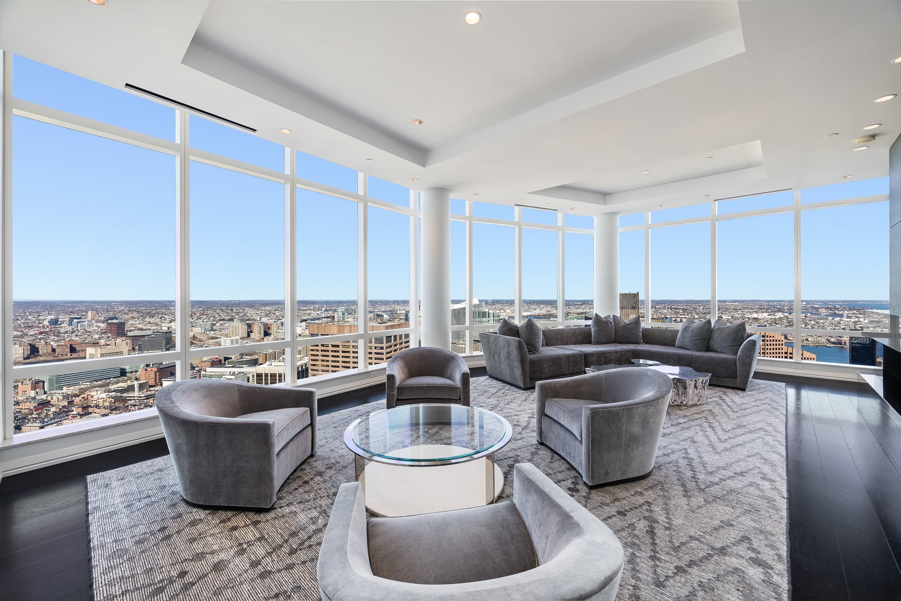 Living room lined with floor-to-ceiling glass walls with view of Boston.