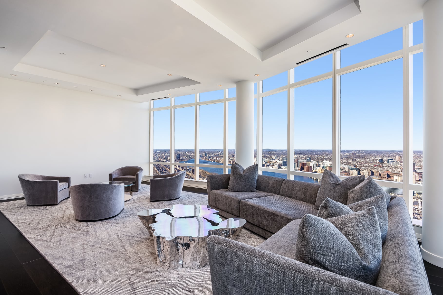 The main living room sits beneath 14-foot ceilings, with floor-to-ceiling glass wrapping the outer walls to frame views of the Boston skyline