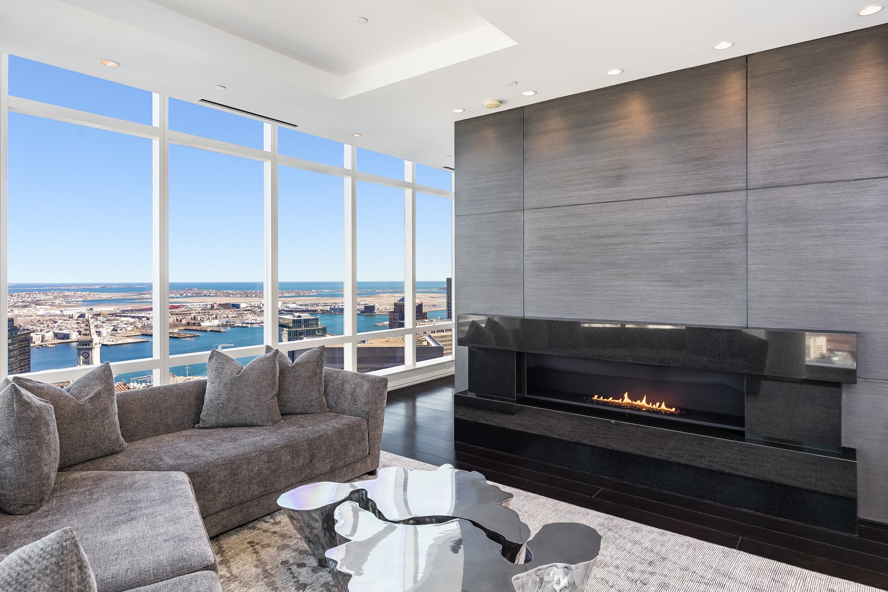 A large gray sofa faces a long gas fireplace set into a dark-paneled wall.