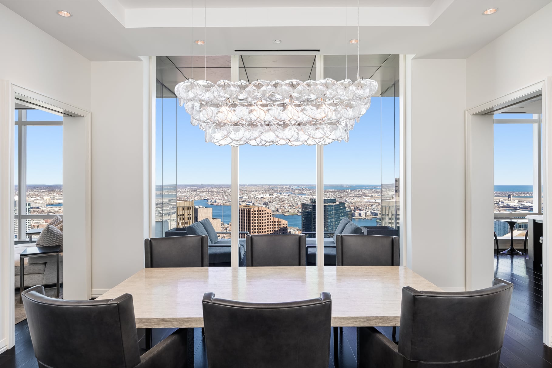 The dining room with six leather chairs placed around a long rectangular table beneath a sculptural glass chandelier.