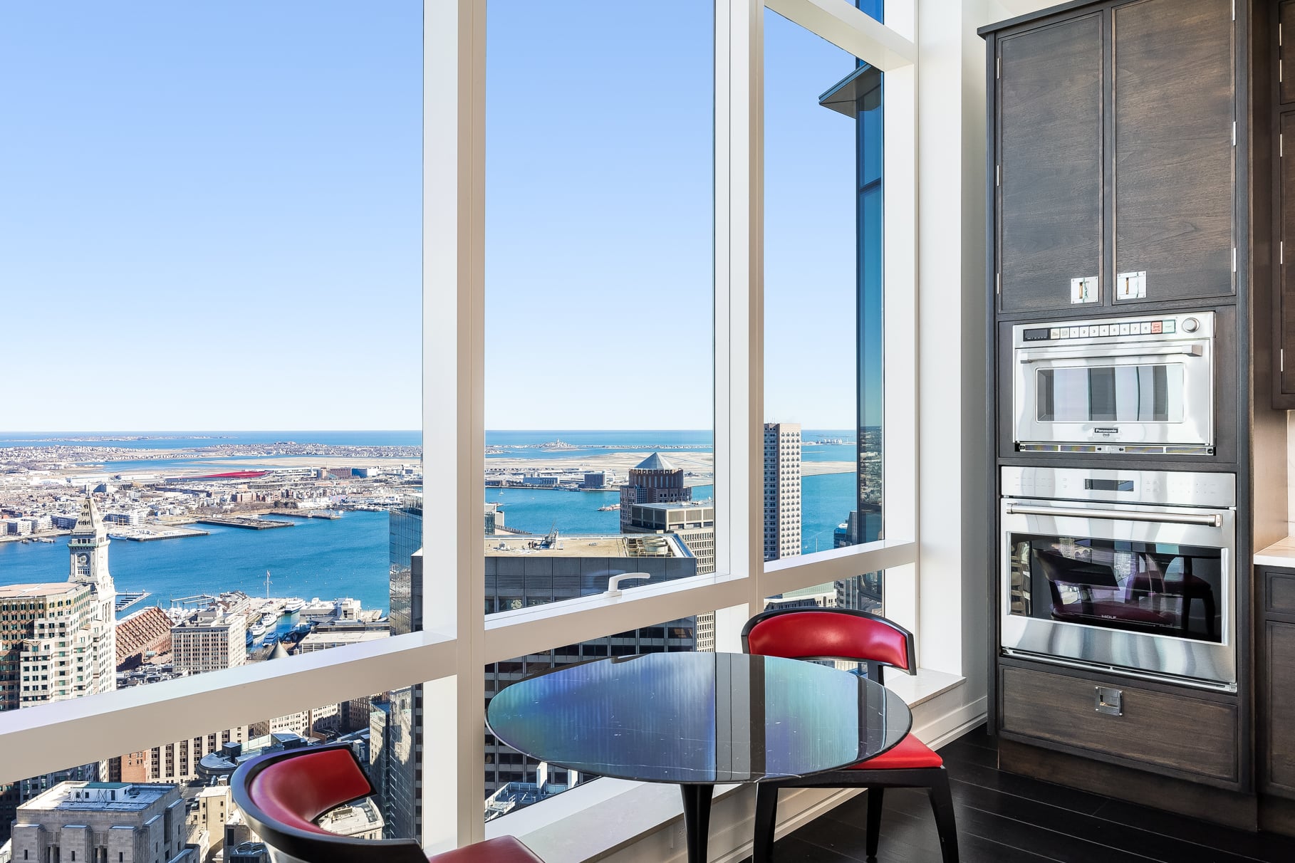 At the far side of the room, a small breakfast area is placed directly against the windows, pairing a round table with harbor views.