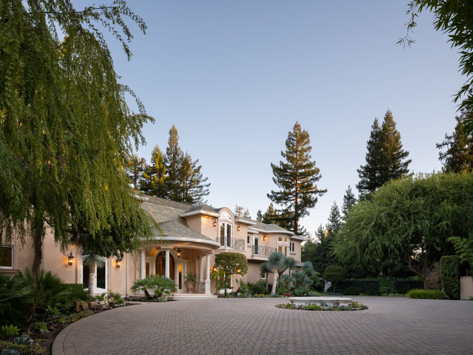 A long, winding stone driveway bordered by mature bamboo and dense Mediterranean-inspired landscaping.