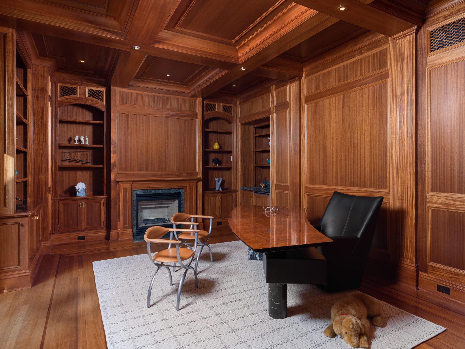 The mahogany-paneled library is wrapped almost entirely in custom millwork, with built-in shelving, paneled walls, and a coffered ceiling.