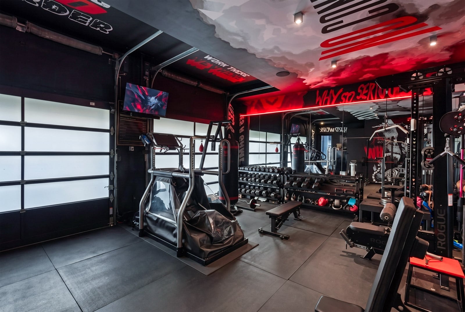 The garage has actually been transformed into the fitness room with mirrored walls, black flooring, and red accent lighting surrounding a full lineup of training equipment.
