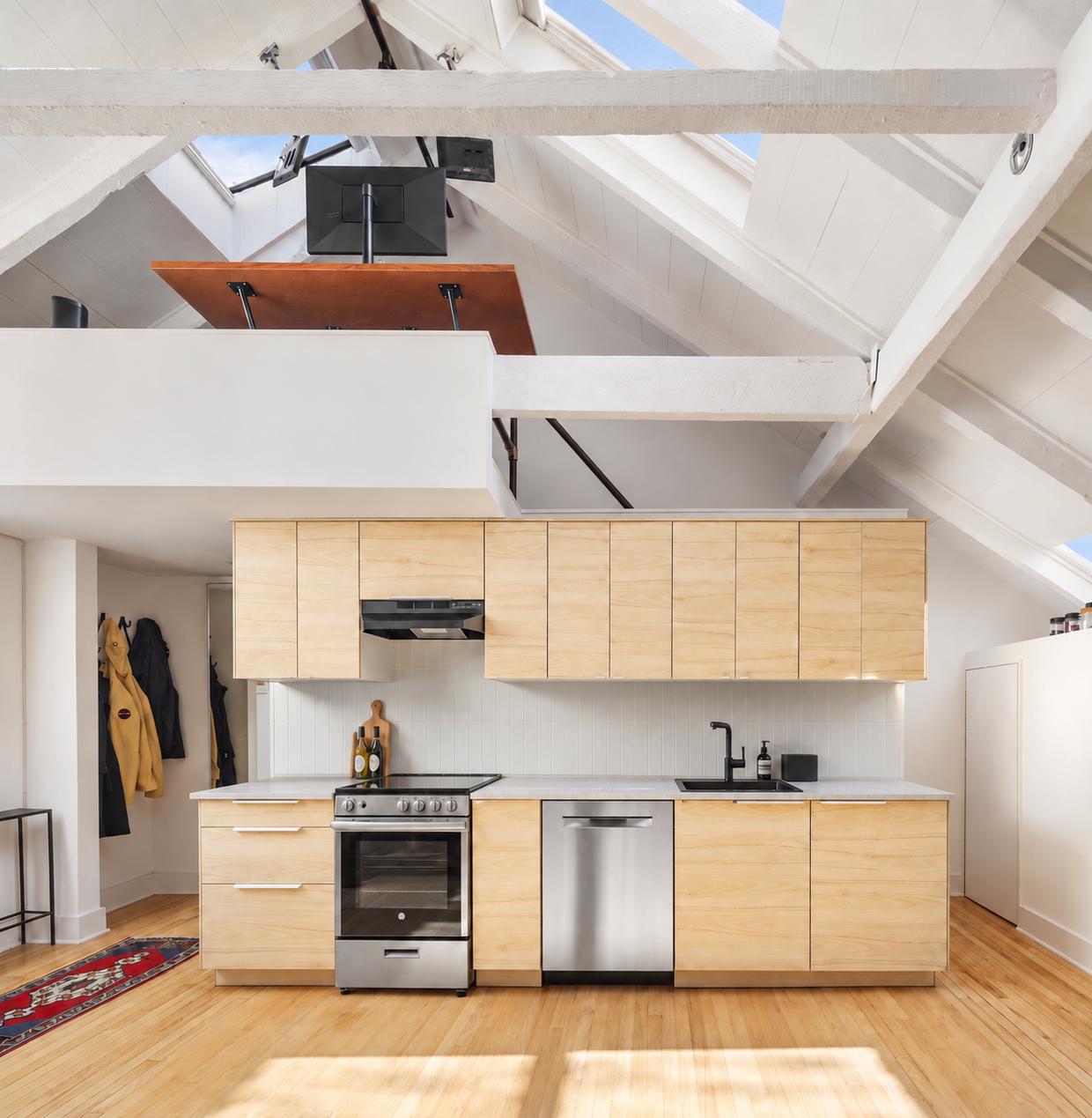 A long run of light wood cabinetry stretches across the wall with the oven set slightly left of center, while the sink and dishwasher continue along the counter to the right.