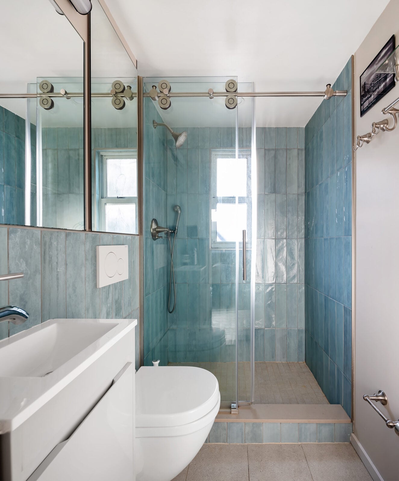 The blue-tiled shower sits at the back of the room behind a sliding glass door, while the single vanity and toilet sit along the opposite side.