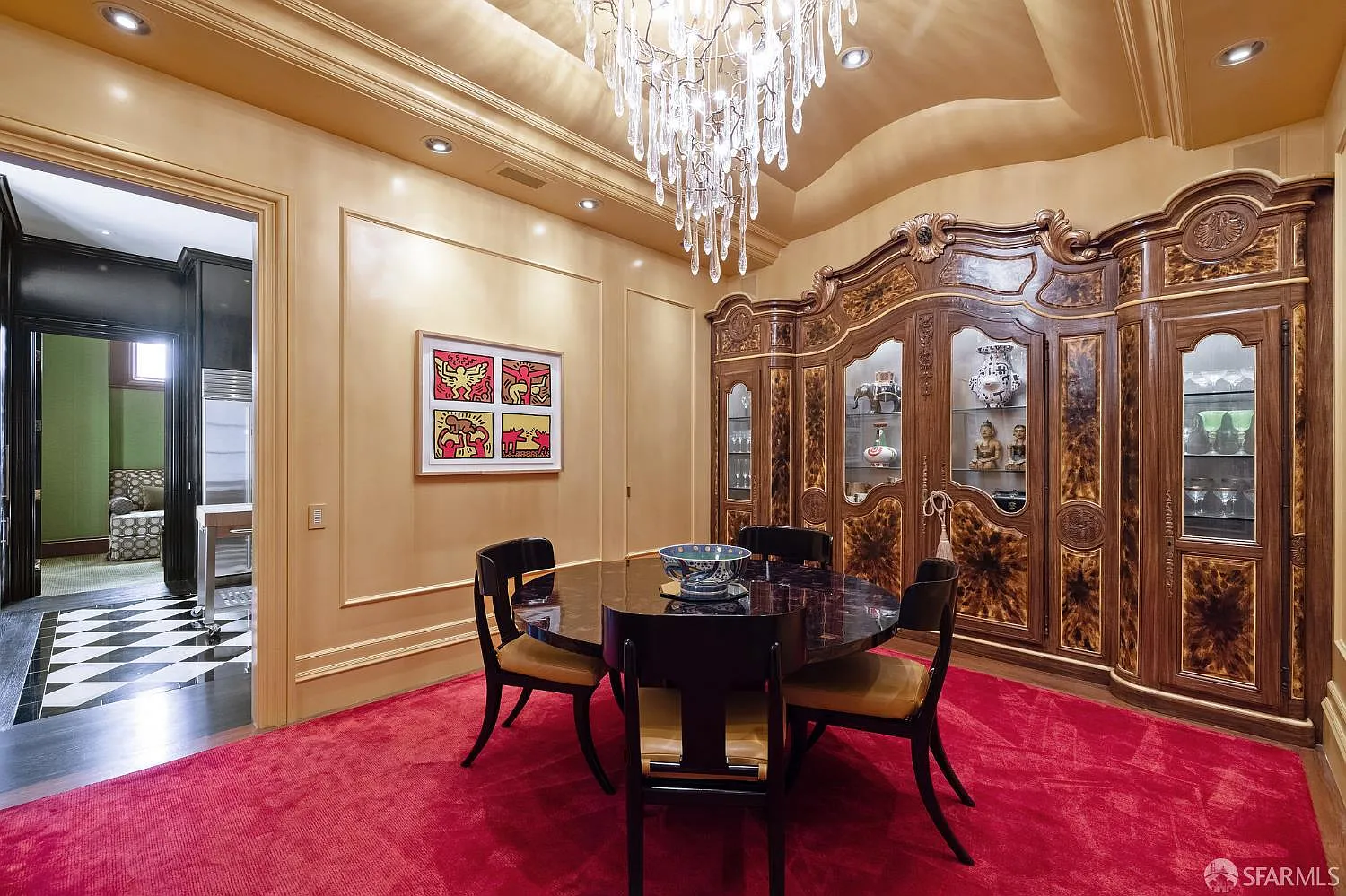 The formal dining room centers on a dark round table atop a deep red rug, with a glass chandelier dropping from the recessed ceiling above. 