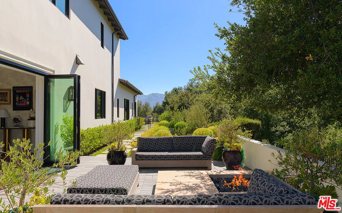Along the side of the house, a separate firepit lounge sits outside the formal living room, with cushioned seating gathered around the flames.