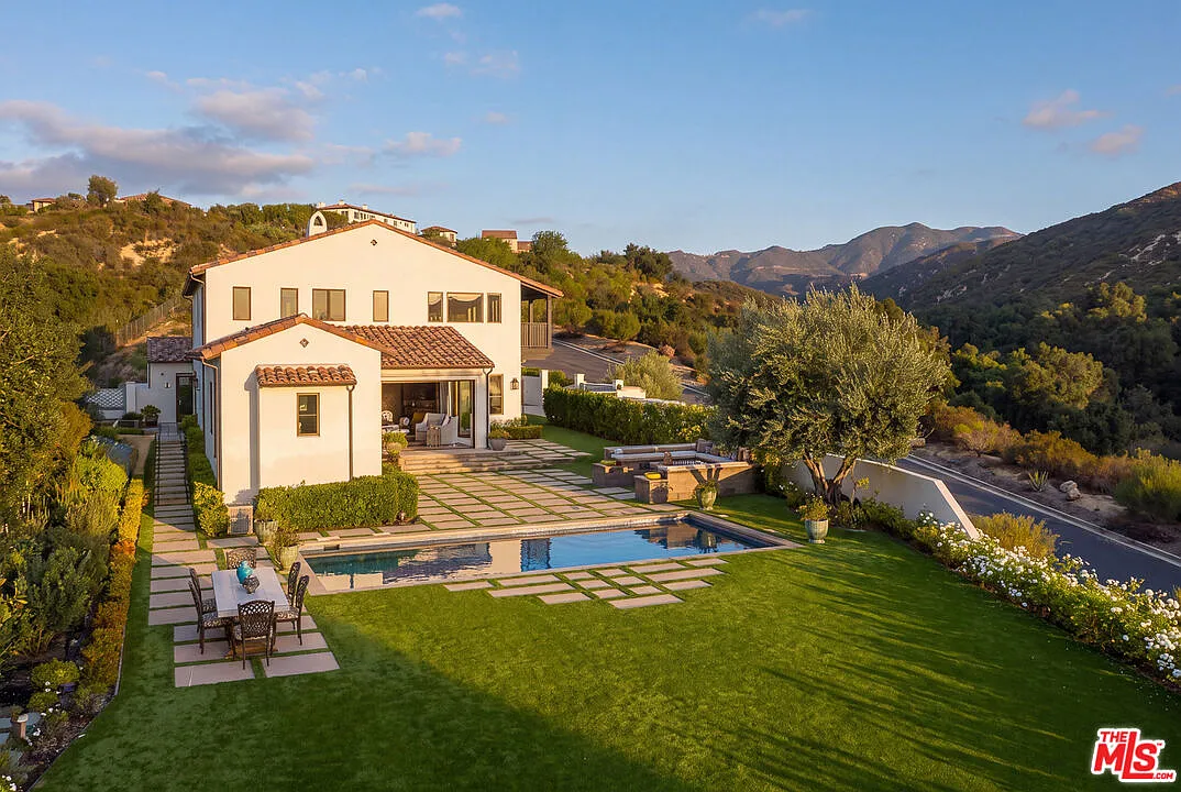 Past the pool, the grounds open into a large lawn framed by flower beds, tall trees, and views of the surrounding Calabasas hills.