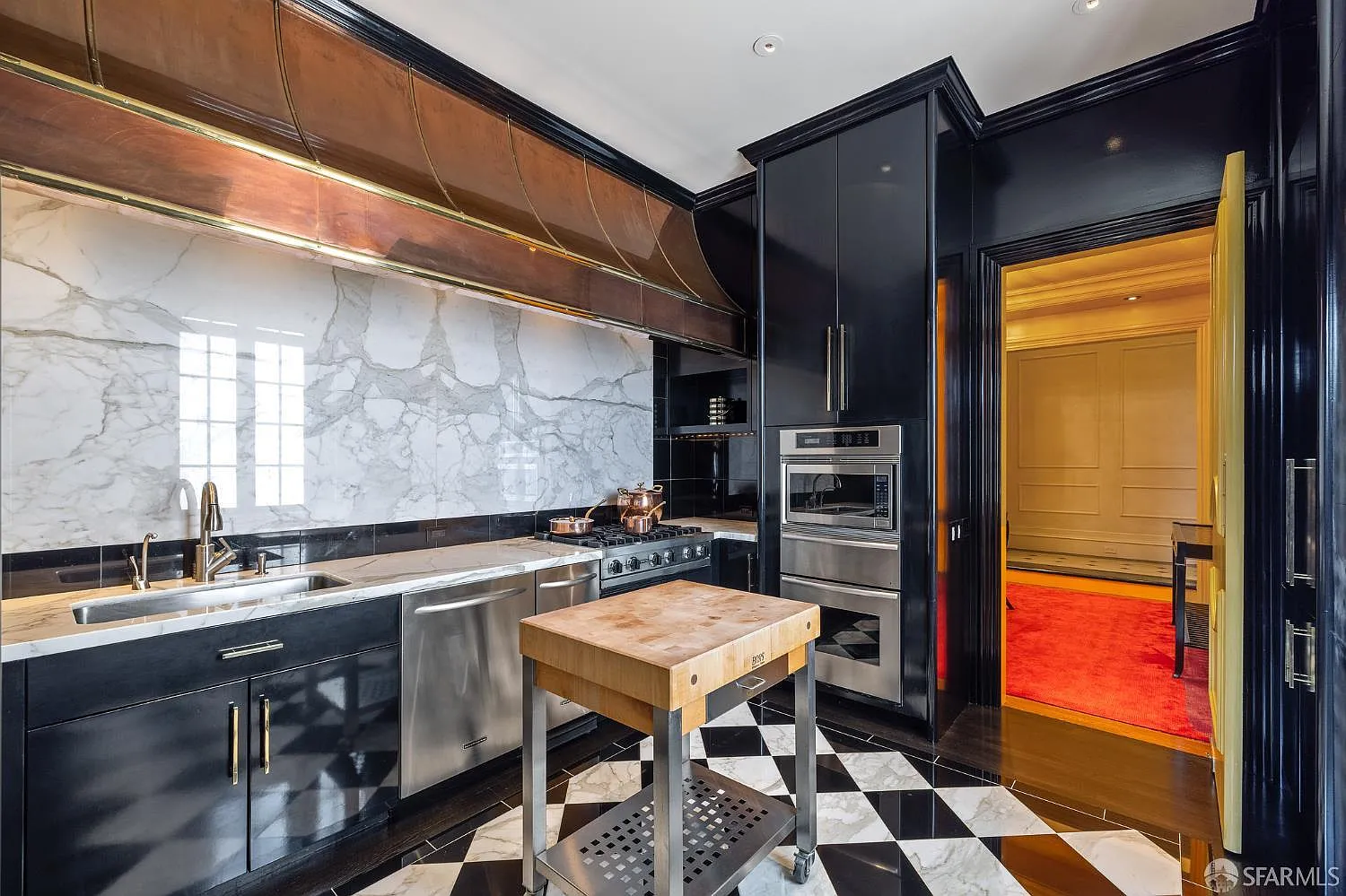 The kitchen shifts into a darker palette, with glossy black cabinetry wrapping the walls around the stainless-steel appliances and stone counters. 