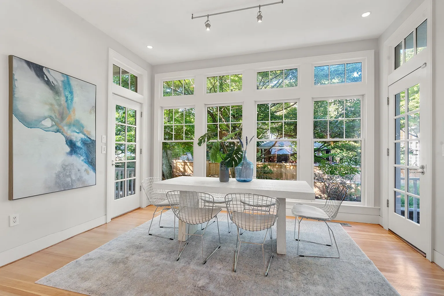 The room opens into a casual dining area surrounded by tall windows and glass doors.