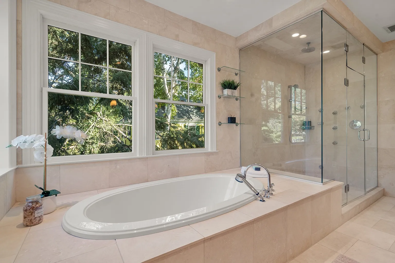 A deep soaking tub sits beneath the windows, while a large glass-enclosed shower is placed ight next to it.